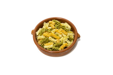 Spiral pasta of three colors, served in a clay bowl. Isolated on a white background.