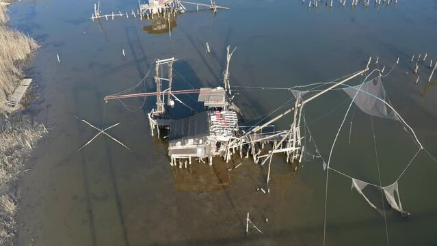 Traditional fishing huts on the river - old-style cabins with raised torn nets on wooden pillars over the Port Milena water canal or lake near Ulcinj Montenegro. Aerial drone view.