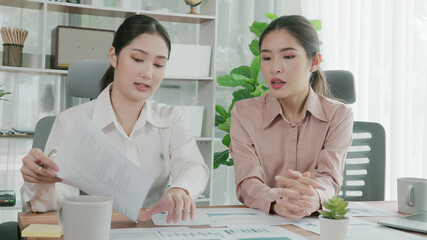 Closeup two young enthusiastic businesswoman working together in the office desk with data chart report papers. Young colleagues discuss and analyzing plans and strategy on statistic data paper.