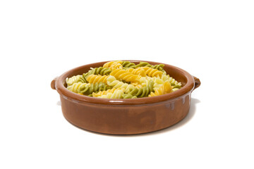 Spiral pasta of three colors, served in a clay bowl. Isolated on a white background.