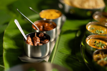 An assortment of traditional Indian seasonings — curry chilis; pickles; and 'gunpowder' splice blend ('milagai podi') — against a backdrop of banana leaves, suggesting southern Indian cuisine.