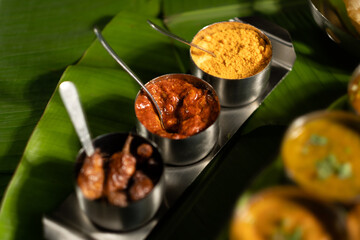 An assortment of traditional Indian seasonings &mdash; curry chilis; pickles; and 'gunpowder' splice blend ('milagai podi') &mdash; against a backdrop of banana leaves, suggesting southern Indian cuisine.