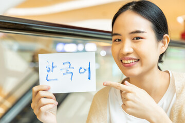 Smiling woman showing Hankul Korean vocab flash card, concept of east asian foreign language...