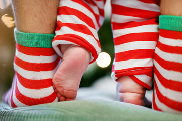 Baby's legs and Dad's legs in Christmas striped socks near the Christmas tree