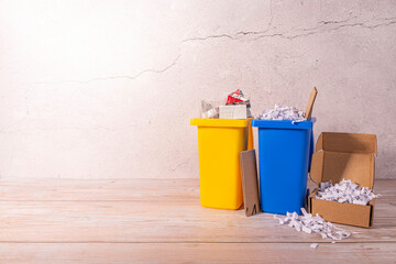 Gelbe und blaue Tonne stehend auf einem Holzboden gefüllt mit Plastik und Papier vor einer hellen Wand mit Riss für Text