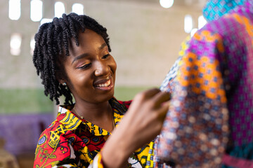 Smiling West African woman dressmaker in her studio - obrazy, fototapety, plakaty