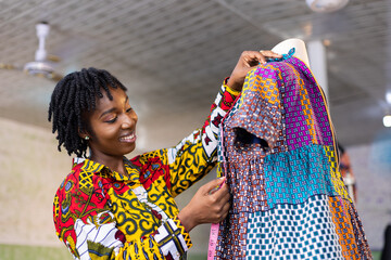 Smiling Ghanaian Dressmaker with locs hair measures a part of her colorful African pattern dress in...
