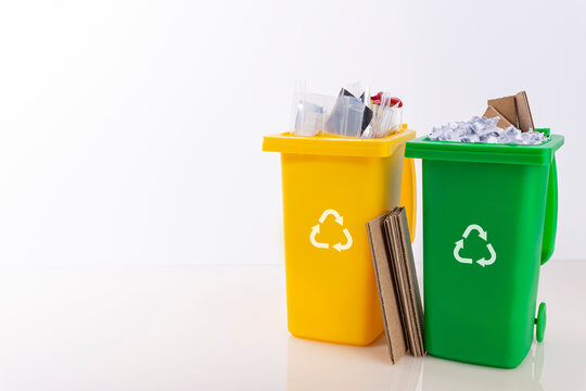 Gelbe und gr&uuml;ne Tonne gef&uuml;llt mit Plastik und Papier vor hellem Hintergrund f&uuml;r Text