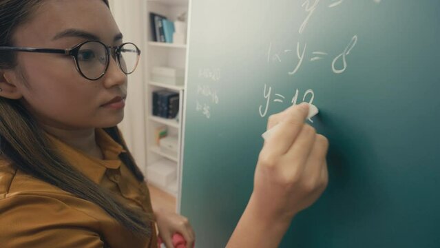 Young Asian woman writing math equations on chalkboard, mathematics teacher