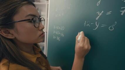 Close-up of focused Asian woman teacher writing equations on board in classroom - Powered by Adobe