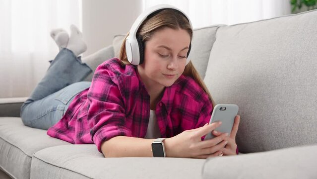 Young woman lying down on sofa and having video call on telephone.