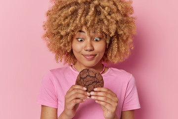 Photo of curly haired young woman holds delicious chocolate cookie feels temptation to eat...