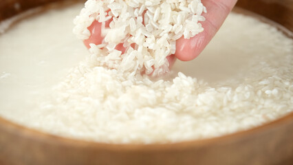 Male washes rice with his hands in a wooden bowl