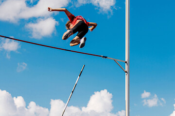 athlete passes bar in pole vault background blue sky