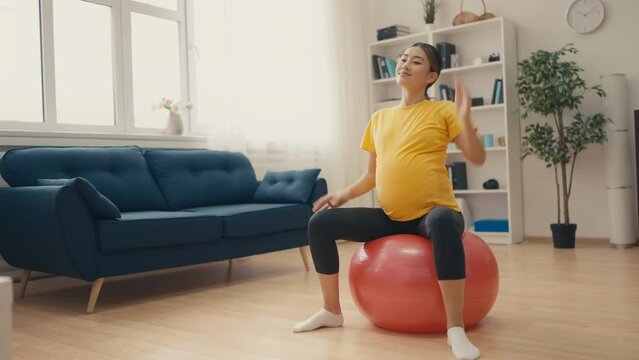 Young smiling pregnant woman doing exercises with fitball at home, healthcare