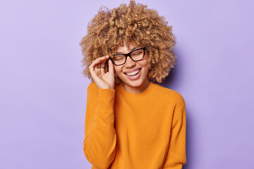Portrait of happy positive European woman with curly hair laughs joyfully expresses happiness keeps...