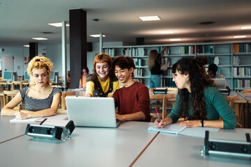 Young university students using laptop and studying with books in library - School education concept
