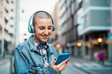 Young girl using mobile smartphone and listening music while waiting for public transportation in the city street - 573240877