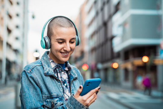 Young girl using mobile smartphone and listening music while waiting for public transportation in the city street
