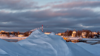 Snow drifts on cityscape background at sunset light.