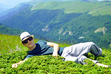 The guy is resting during a mountain hike, lying among the greenery on a sunny summer day.  Holiday...