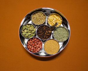 Indian spices and herbs in a container box masala dabba on an orange background, top view