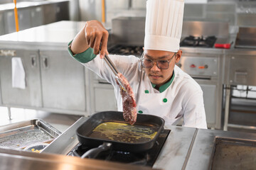Portrait Asia young man in chef uniform cooking steak fire at kitchen	