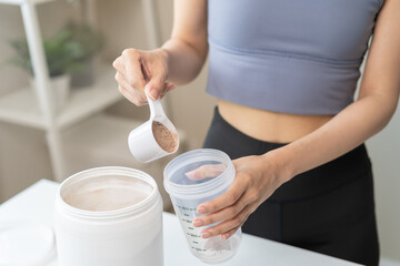 Fototapeta na wymiar Diet meal replacement for weight loss, asian young woman in sportswear, hand in holding scoop making protein into bottle to shake, drink supplement for muscle after workout at home. Healthy body care.