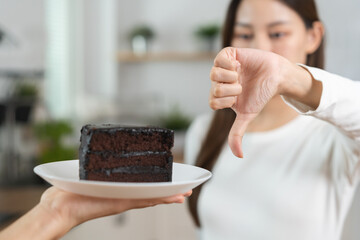 Diet asian young woman hand showing thumb up refusing to eat the chocolate cake or sweet taste,...