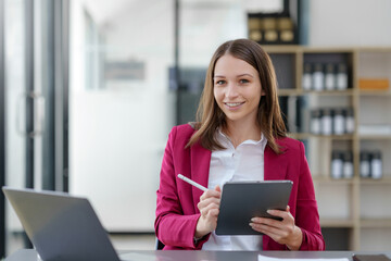 Attractive Asian businesswoman sitting happily using tablet at work and smiling happily.