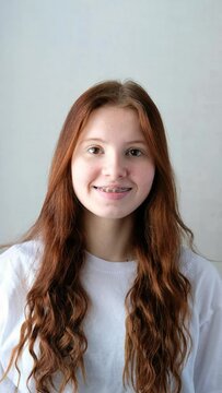 smile of a long-haired red-haired girl in braces in a white t-shirt on a white background