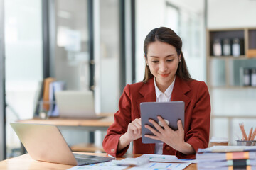 Attractive Asian businesswoman sitting happily using tablet at work and smiling happily.