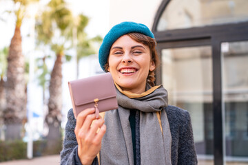 Brunette woman holding a wallet at outdoors with happy expression