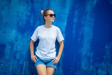 Female model wearing white blank t-shirt on the background of an blue wall.