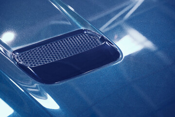 detail of sport car with blue metal hood and air flow intake ornament