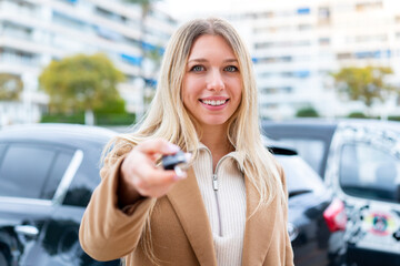 Young pretty blonde woman holding car keys at outdoors