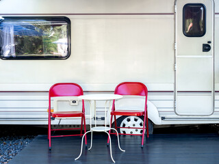 Two empty red iron chairs with white round table in front of the door and window of caravan car with nobody. Relaxation camping and sleep in the motorhome trailer. Family vacation travel concept.