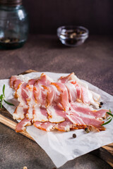 Raw smoked bacon and rosemary on a cutting board on the table. Hearty snack. Vertical view