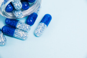 A transparent glass jar with vitamins in tablet form on a blue paper background