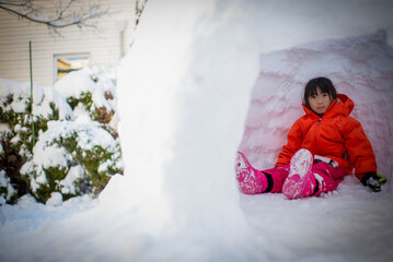 Young asian girl sitting inside igloo built after snow blizzard