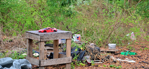 BANGKOK, THAILAND - February 20, 2023 : A damaged red luxury sports car model sits on a wooden table inside the forest with natural background.