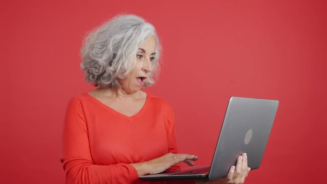 Surprised mature woman standing and using a laptop
