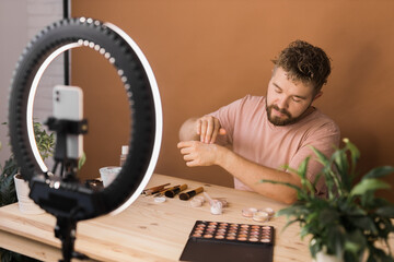 Man recording video vlog while applying cosmetics or explore cosmetic product. Guy making tutorial make-up for his blog on cosmetics.