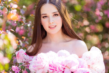 Close up of smiling beautiful girl holding a large bouquet of pink peonies