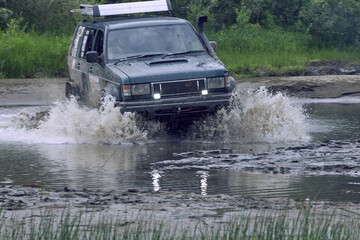 Off-road 4x4 car overcomes a ford at high speed, splashes from under the wheels when moving across...