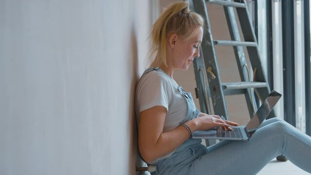 Woman renovating room at home sits on floor with laptop taking a break from decorating room - shot in slow motion