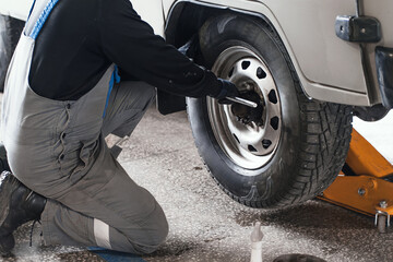 Man changes wheel of car in car service. Professional auto mechanic in overalls removes wheel from...