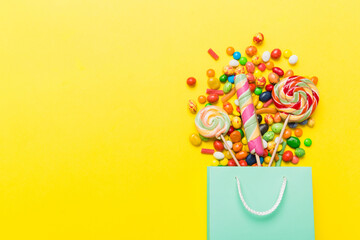 shopping paper gift bag in corner full of assorted traditional candies falling out on colored background with copy space. Happy Holidays sale concept