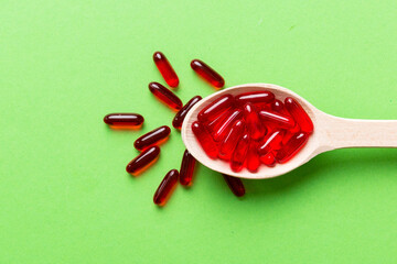 Vitamin capsules in a spoon on a colored background. Pills served as a healthy meal. Red soft gel vitamin supplement capsules on spoon