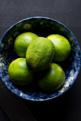 Top view of green limes in a bowl with dark background